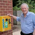 Mervyn instigated Hatley having a defibrillator, which was installed outside the village hall in late 2018 – he is pictured here with it on 14th July 2022 – from memories of Hatley, by Mervyn Lack, July 2022. Photo: Peter Mann.