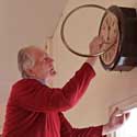 Mervyn Lack winding the clock in Hatley Village Hall – Mervyn had it repaired after years of it not going properly (most not at all!) on 14th July 2022 – from memories of Hatley, by Mervyn Lack, July 2022. Photo: Peter Mann.