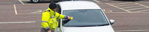 A civil parking enforcement 'service agent' putting a parking ticket on a car – part of Cambridgeshire County Council's take over of parking enforcement - March 2023.